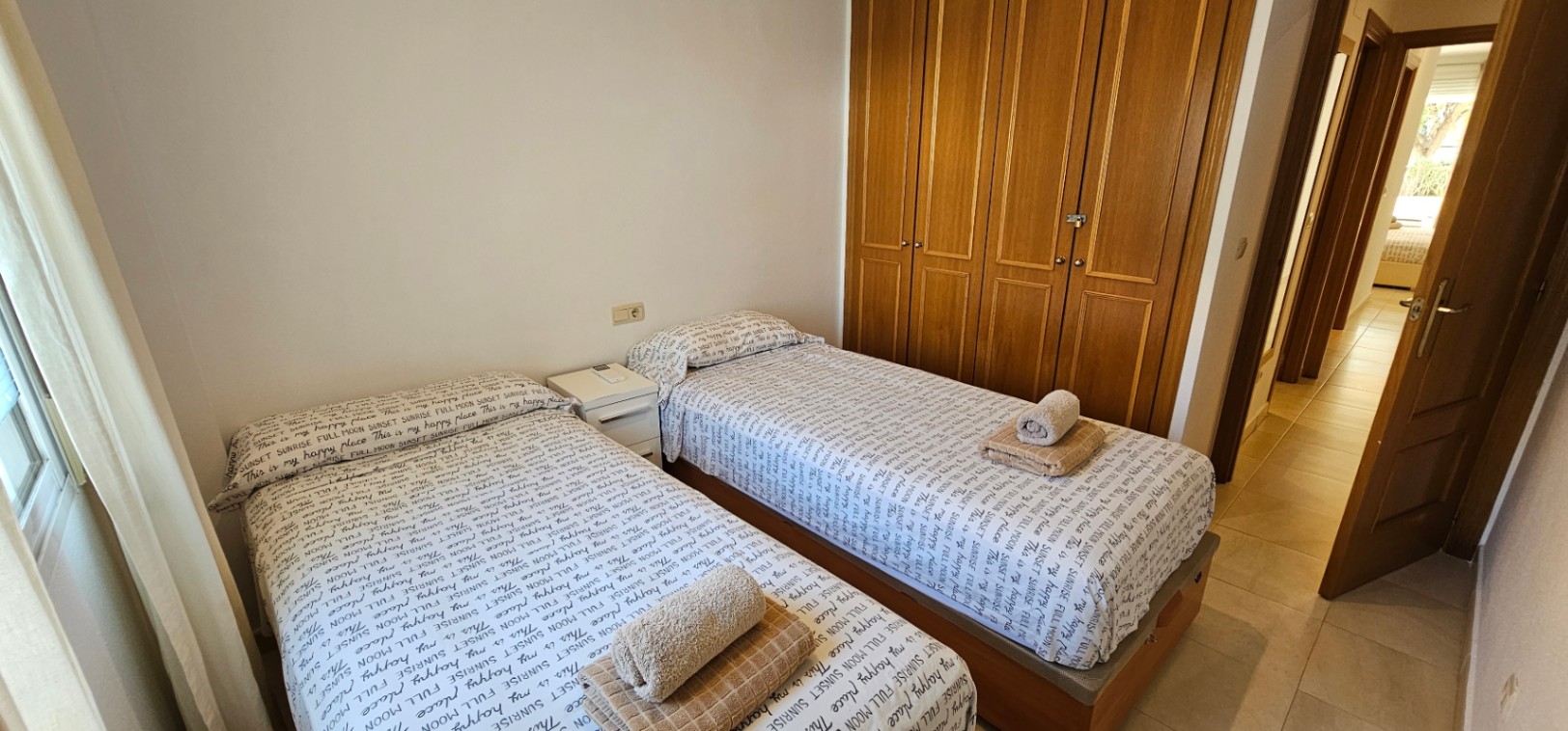 Bedroom featuring twin single beds, a large four-door built-in wooden wardrobe, and light-toned ceramic tile flooring.