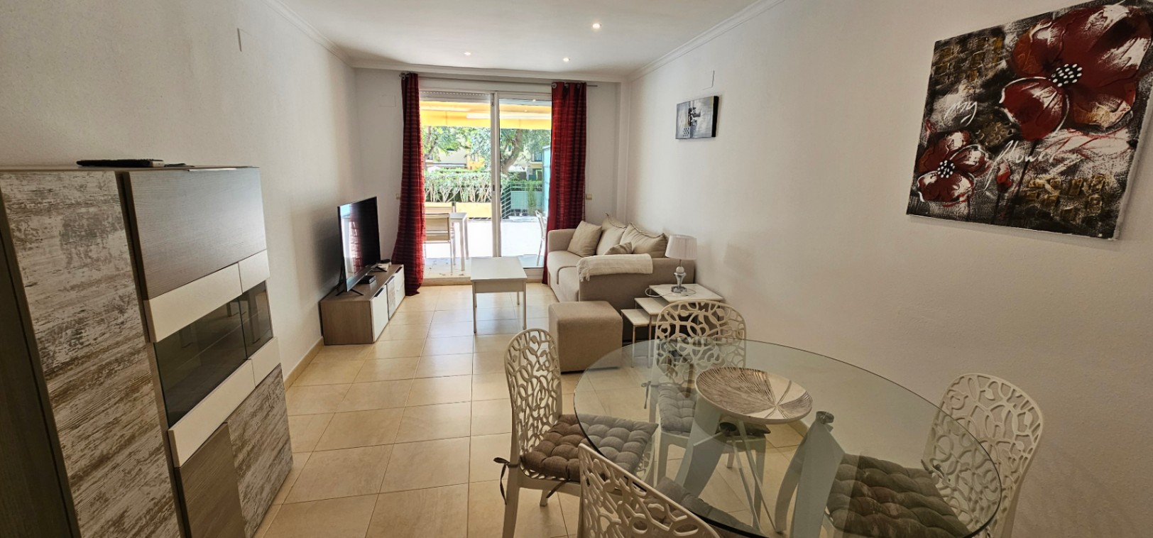 Bright living-dining area featuring ceramic floors, a glass table, beige sofa, and direct access to a private terrace through sliding glass doors.