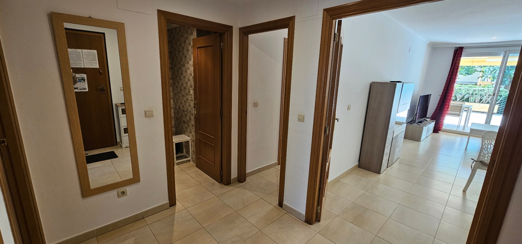 Entrance hallway featuring light tiled flooring and wooden door frames, providing access to a mosaic-tiled bathroom and the bright living area.