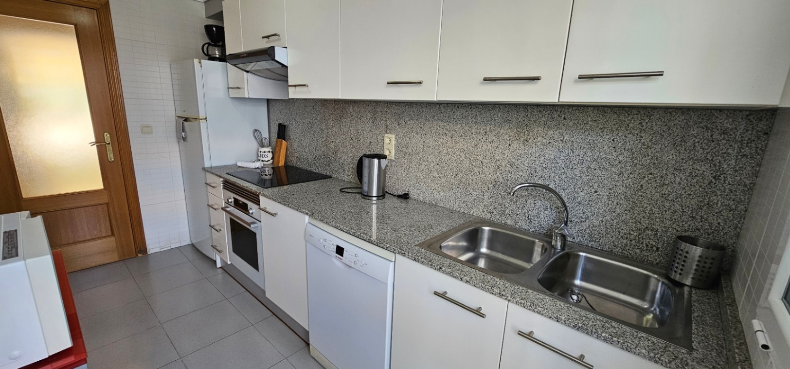 Equipped kitchen featuring white cabinetry, grey granite countertops, integrated appliances, and a double stainless steel sink.