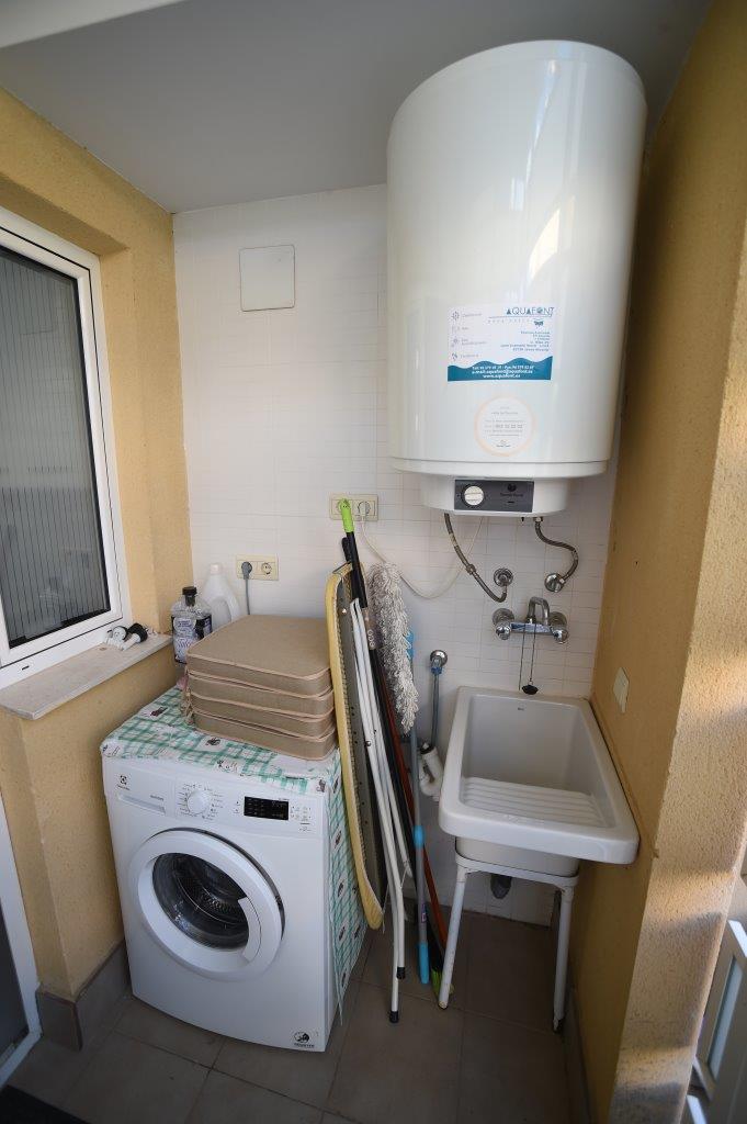 Functional utility area featuring a washing machine, a large electric water heater, a laundry sink, and dedicated storage for cleaning tools.