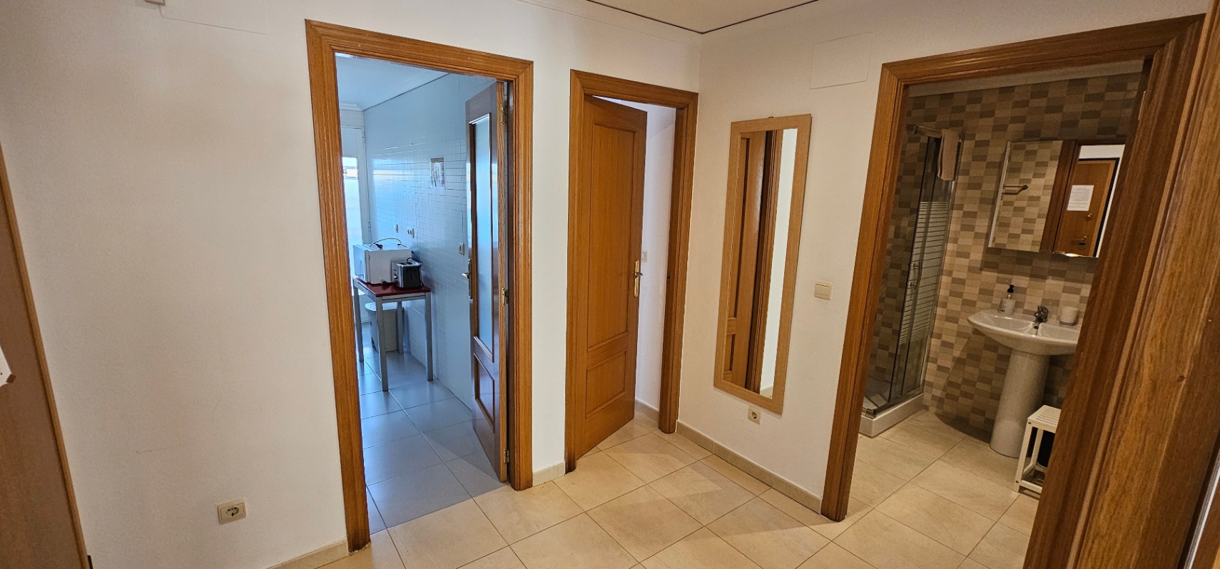 Hallway with ceramic flooring connecting the kitchen, a bedroom, and a bathroom featuring a walk-in shower and tiled walls.