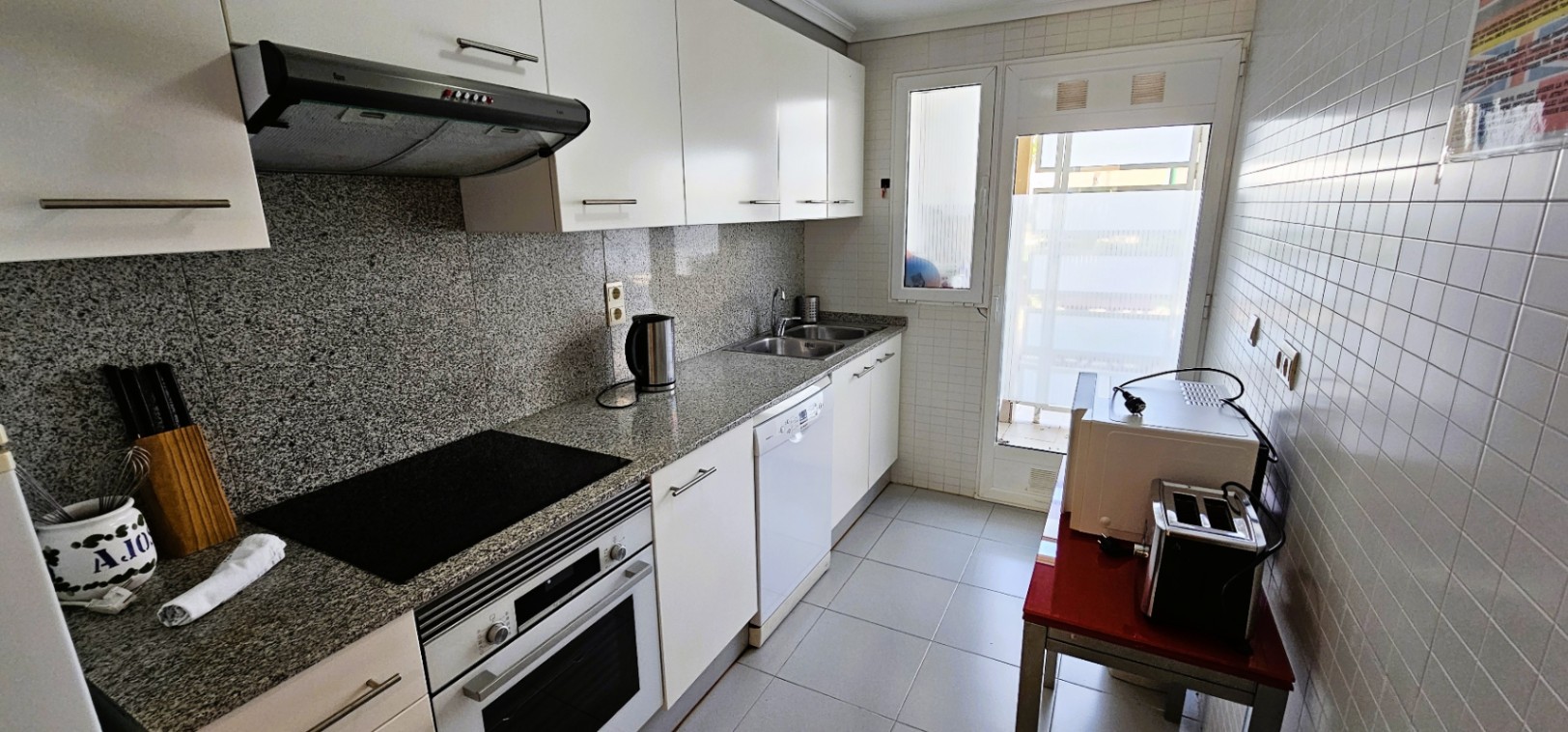 Independent kitchen featuring granite countertops, white cabinetry, and integrated appliances. A glass door provides natural light and access to the utility area.