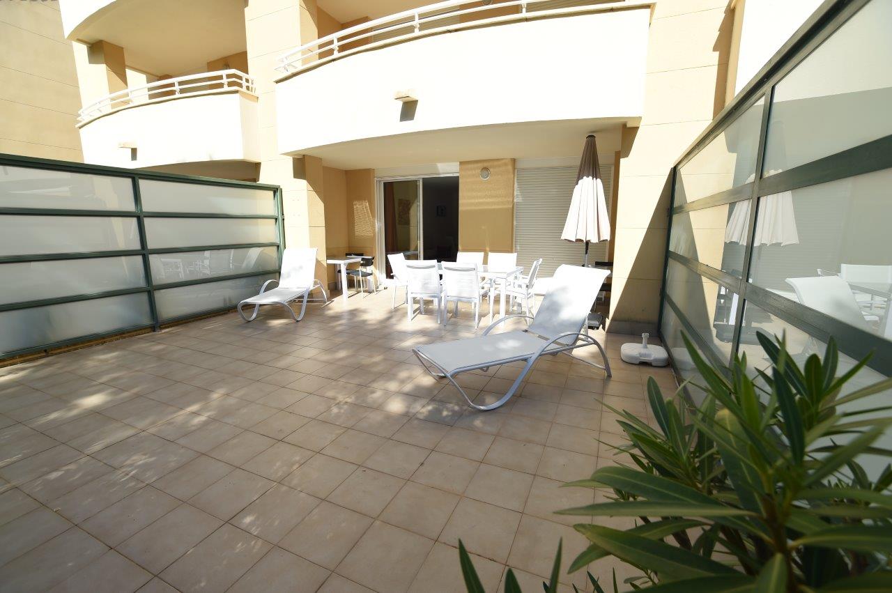 Private ground floor terrace featuring ceramic tiling, white sun loungers, and an outdoor dining area sheltered by the building's overhang.