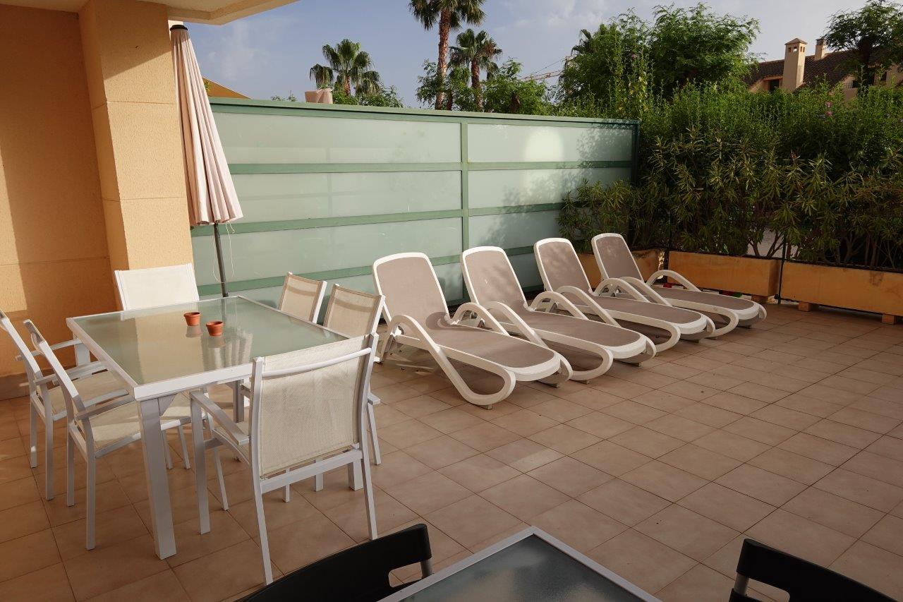Private tiled terrace featuring an outdoor dining set with a glass-top table, multiple sun loungers, and frosted glass privacy screens bordered by greenery.