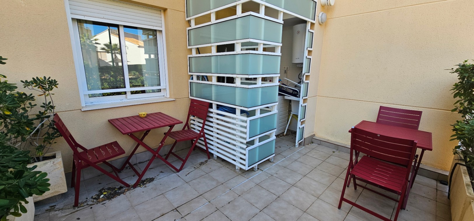 Private tiled terrace featuring burgundy folding furniture and a white utility enclosure with frosted glass panels for the laundry and water heater area.