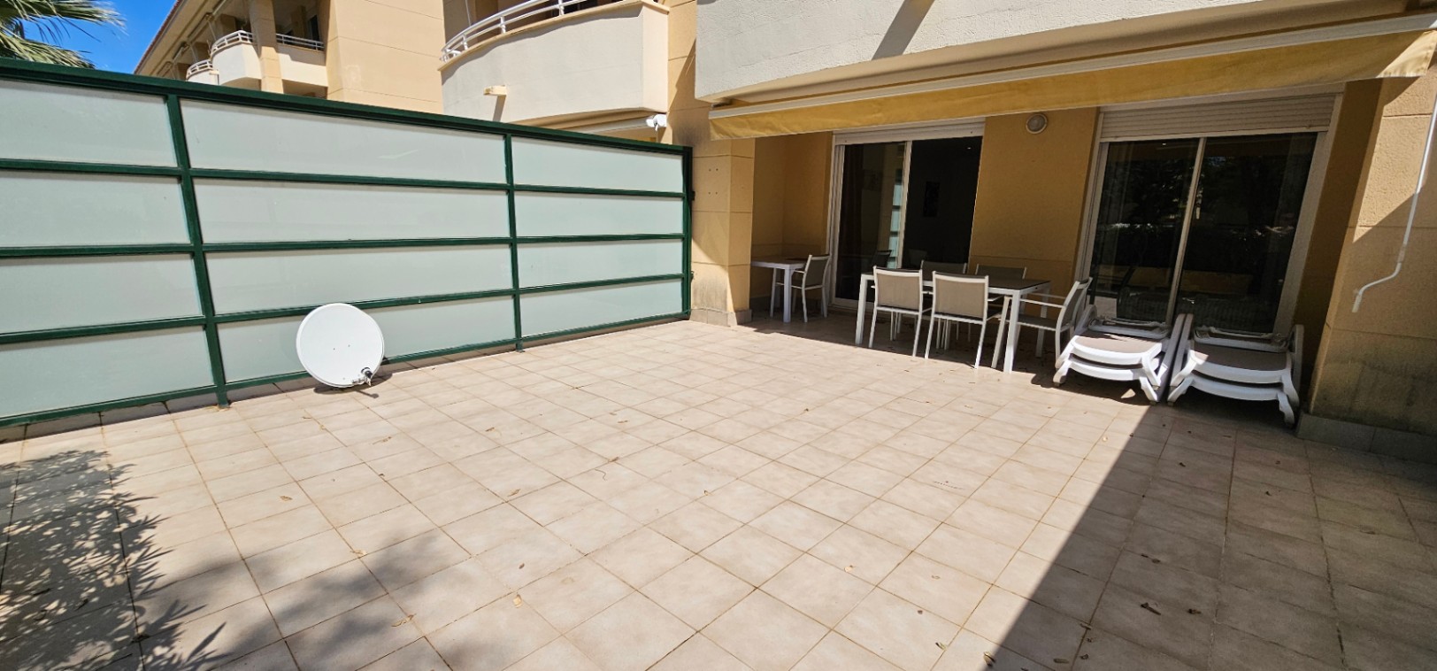 Spacious ground-floor terrace featuring ceramic tiling, a shaded dining area under a yellow awning, and translucent privacy screening.