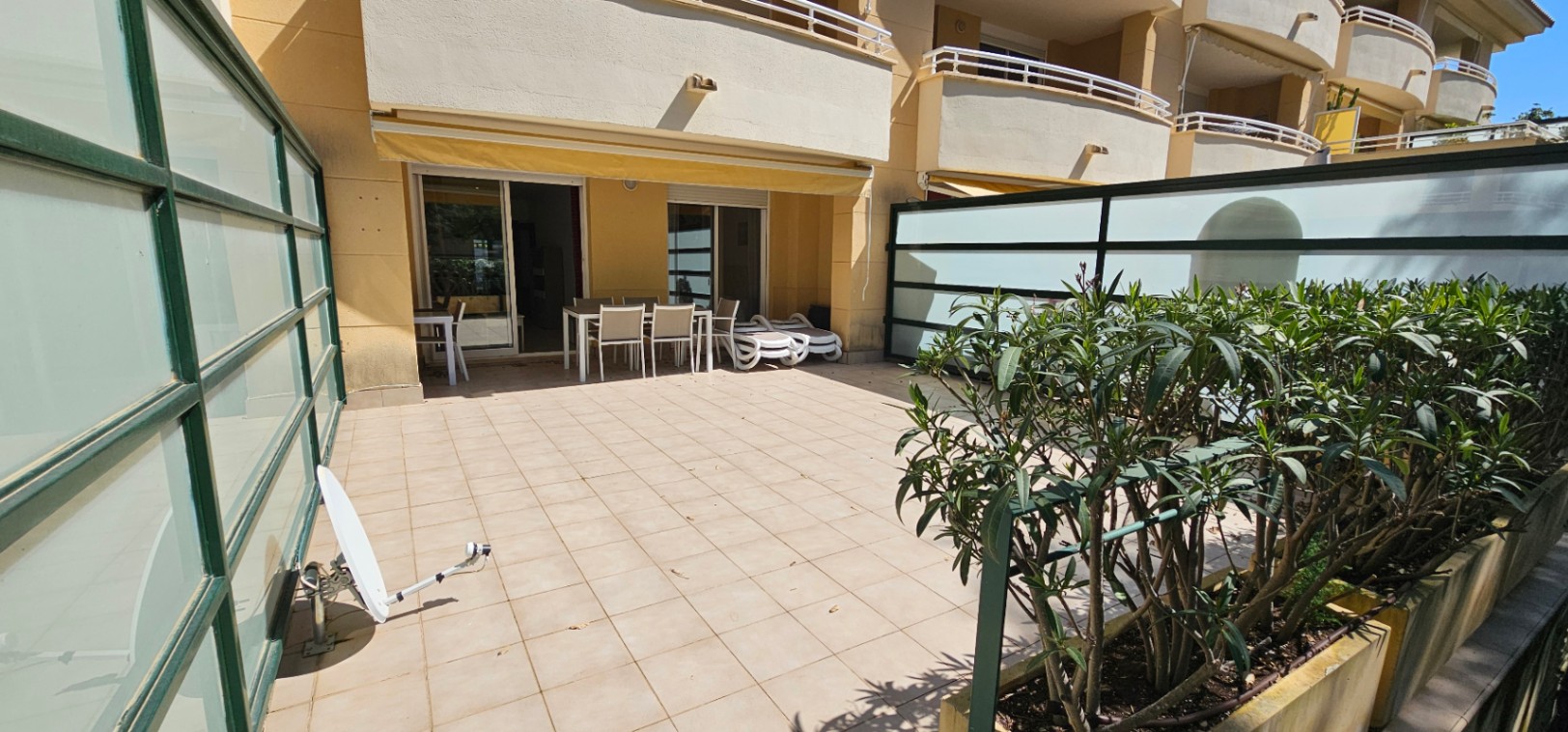 Spacious ground-floor terrace featuring tiled flooring, outdoor dining furniture, sun loungers, and frosted glass privacy screens under a retractable awning.