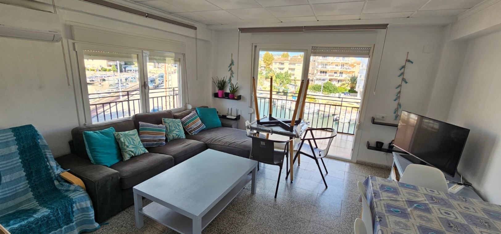 Bright living area featuring a large corner sofa, air conditioning, and sliding doors opening onto a terrace with views of the marina canal.