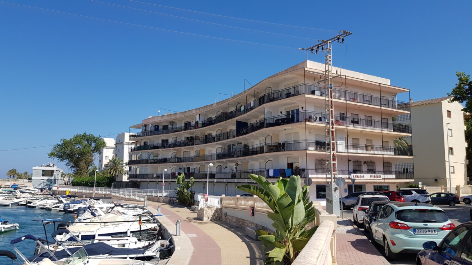 Curved residential building overlooking the marina, featuring continuous wrap-around balconies and a prime waterfront location near the boat moorings.