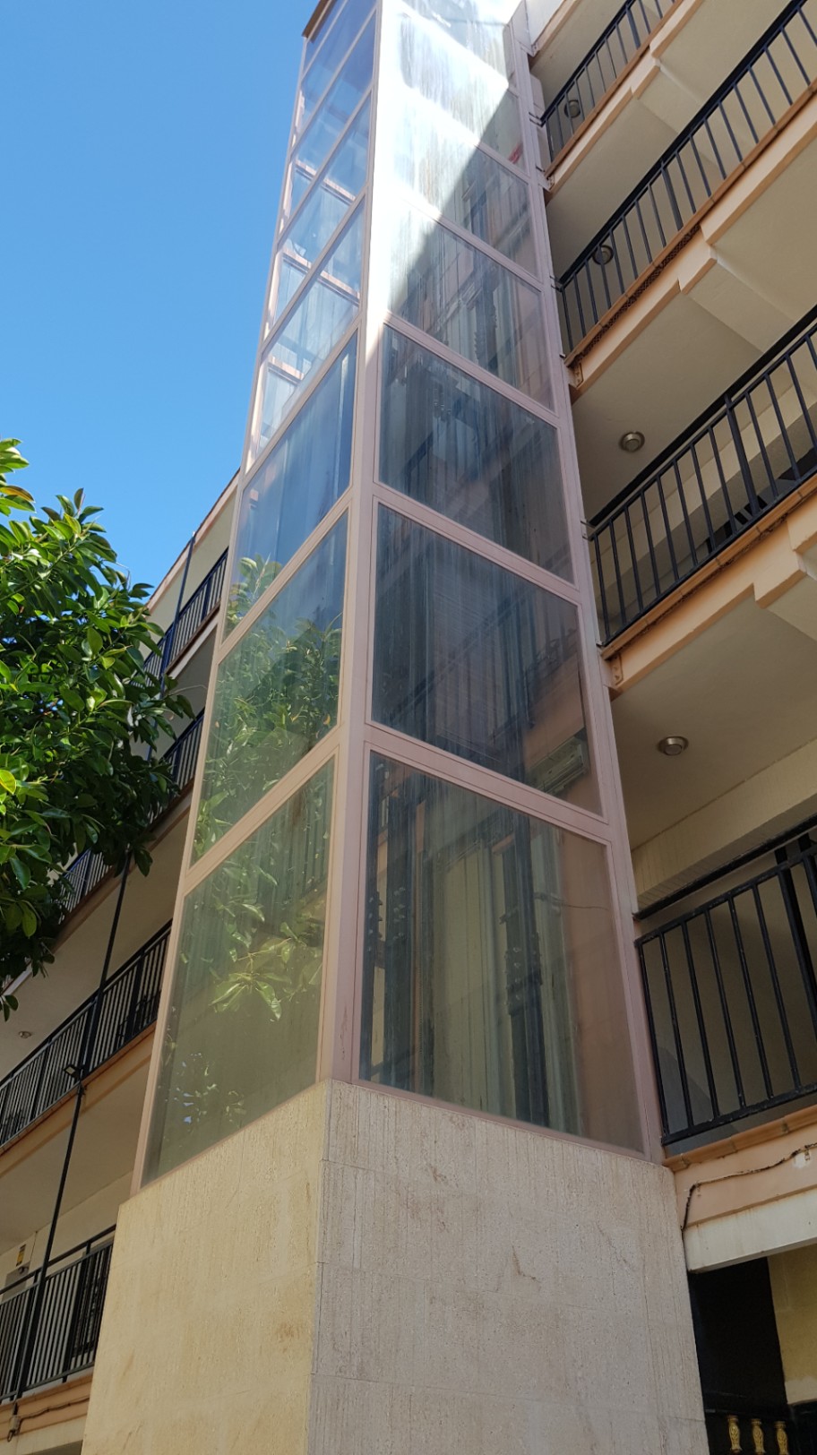 External panoramic glass elevator with a metal frame, providing access to the various levels of the building alongside the private balconies.