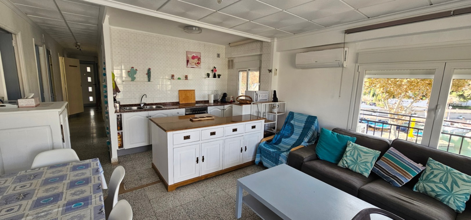 Open-plan living area featuring a white kitchen with a central island, integrated air conditioning, and large windows overlooking the marina.