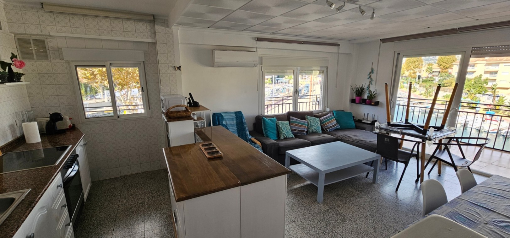Open-plan living area featuring an integrated kitchen with a wooden island and direct access to a balcony overlooking the marina and canal.
