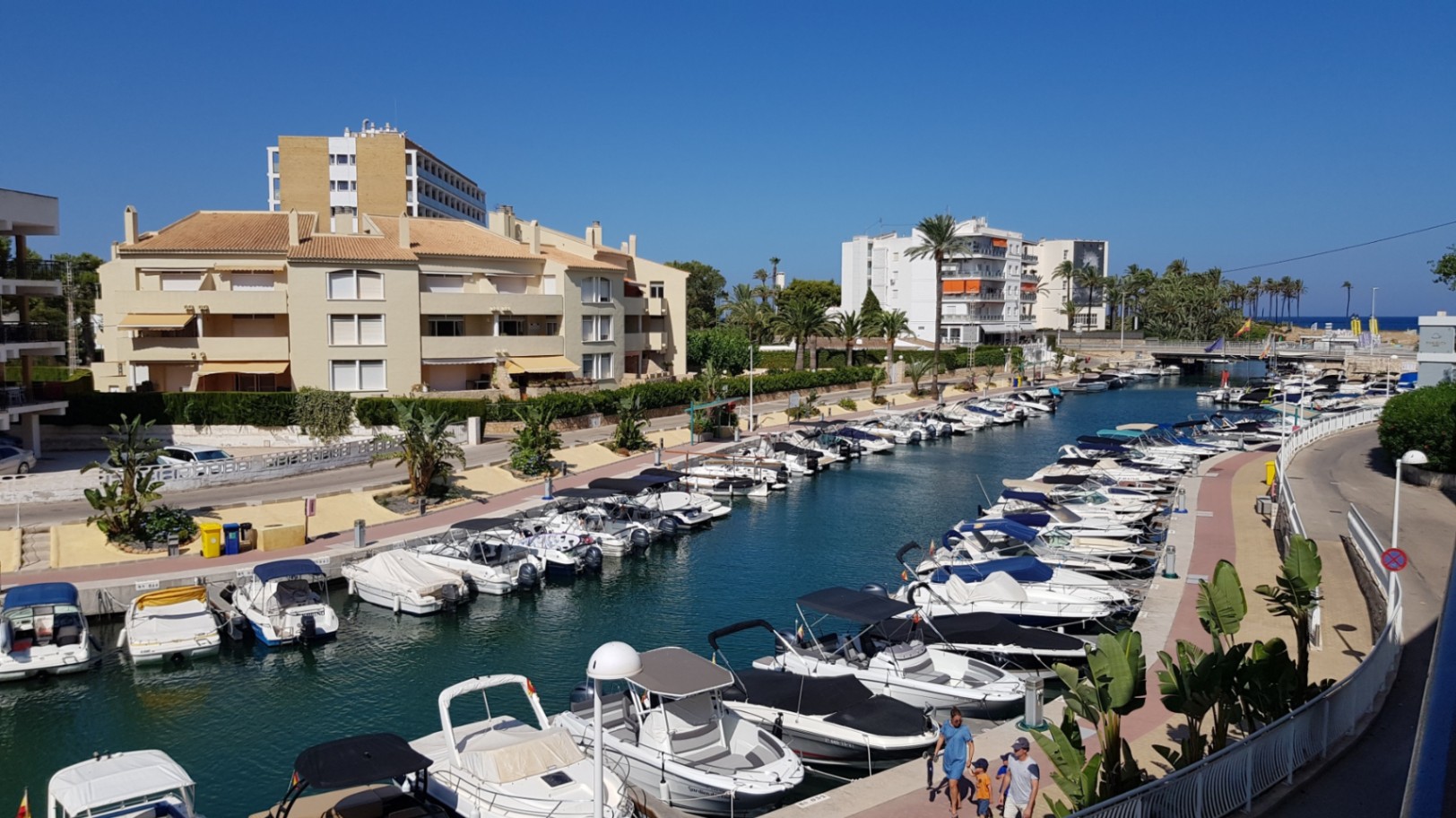Panoramic views from the terrace overlooking the marina canal, featuring moored leisure boats and residential architecture under a clear blue sky in Jávea.