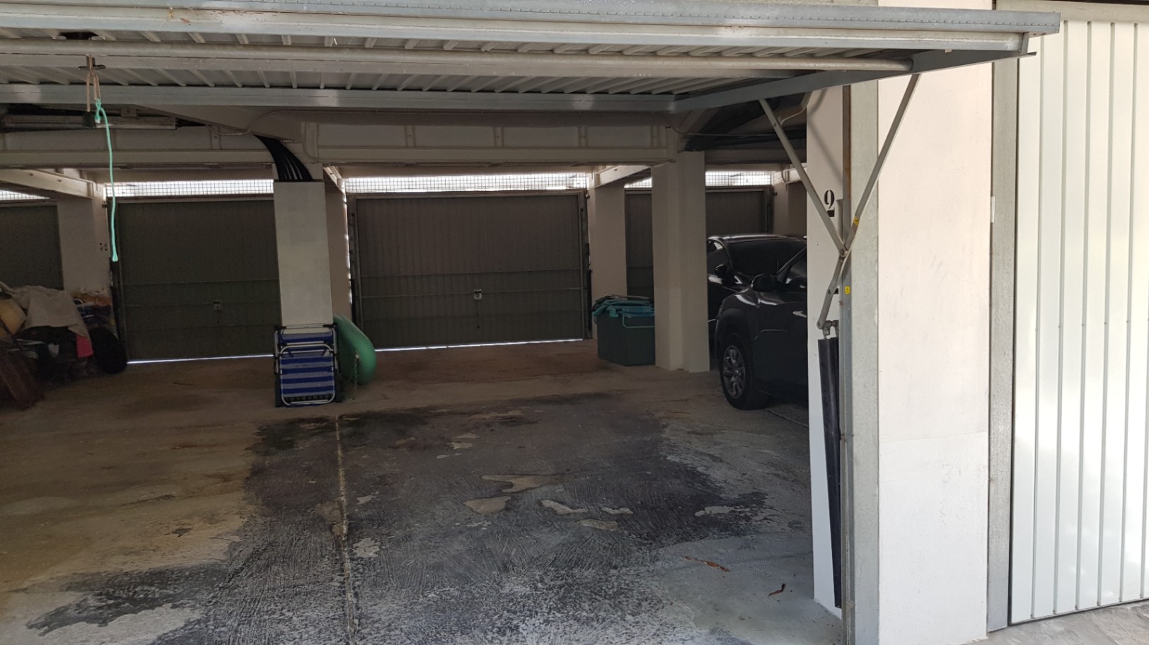 Private garage bay featuring a metal up-and-over door and concrete flooring, located within a secure covered parking area.