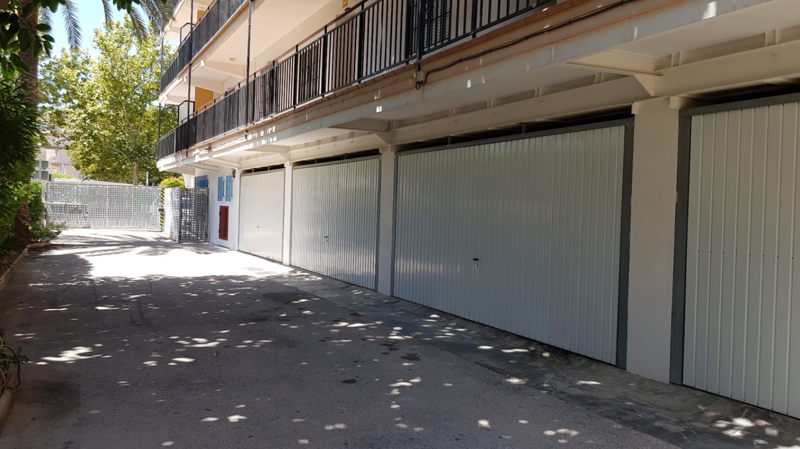 Private individual garage units with white metal doors, located on the ground floor of the building with direct access from a paved, shaded driveway.