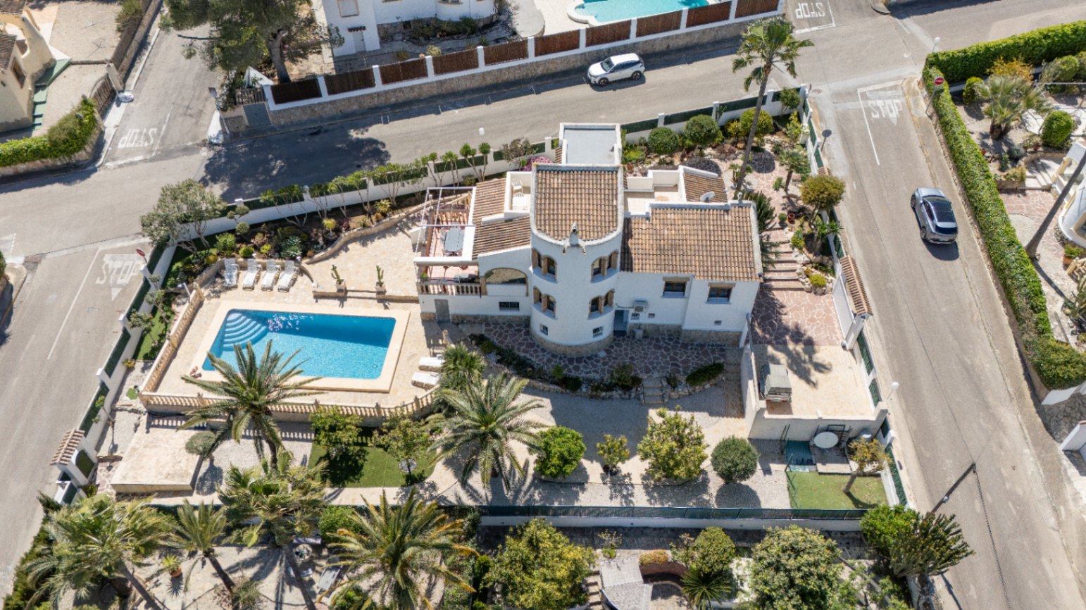 Aerial view of the property on a corner plot, showcasing the rectangular pool, circular tower, and Mediterranean garden with palm trees.