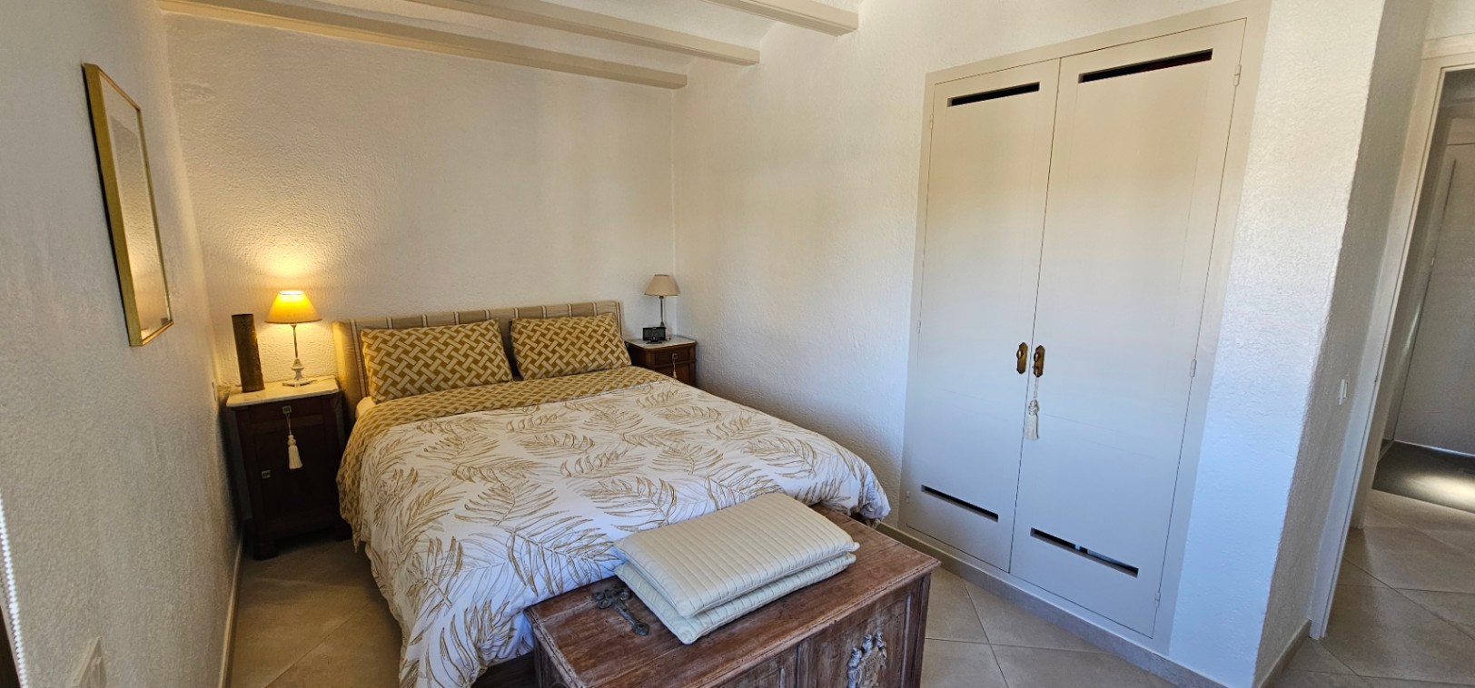Bedroom featuring exposed ceiling beams, a built-in double wardrobe, and a rustic wooden chest at the foot of the bed.