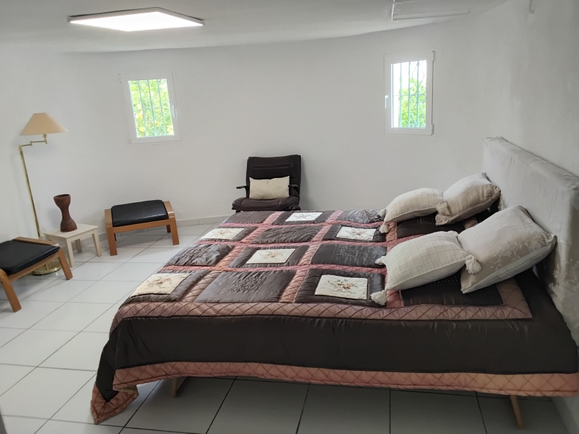 Bedroom featuring white tiled flooring, a double bed, and auxiliary seating. The space includes security-barred windows and a modern flat LED ceiling light panel.