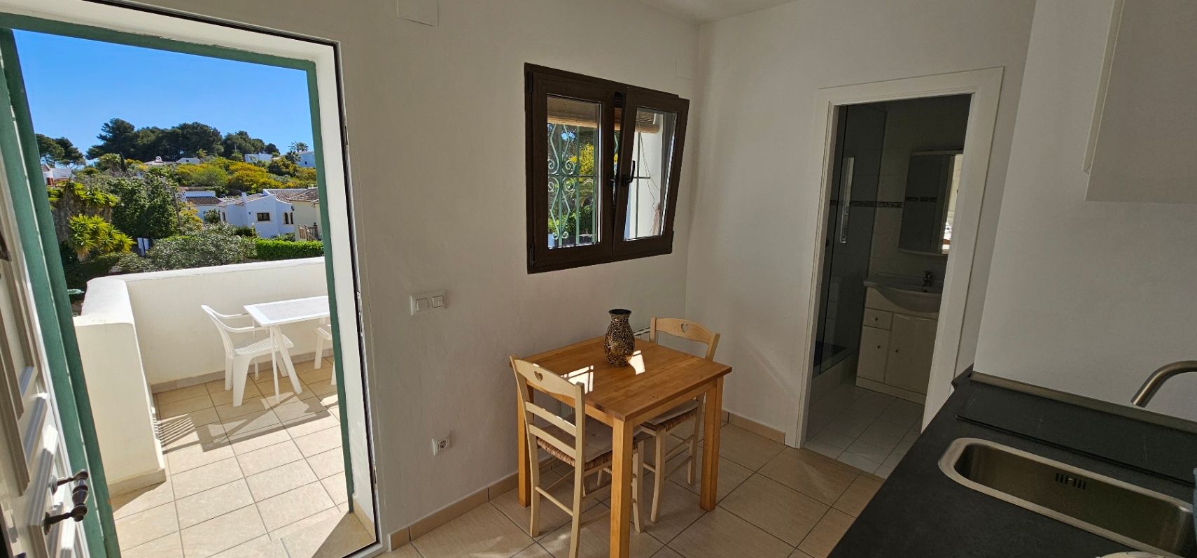 Dining space with a wooden table, direct access to a private terrace, and a view of the adjacent bathroom and kitchen counter.