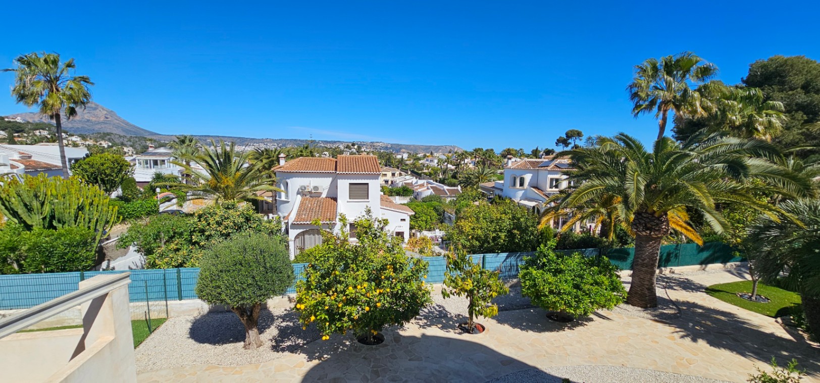 Elevated terrace view showcasing the Mediterranean garden with lemon trees and palms, with the Montgó mountain visible in the distance.
