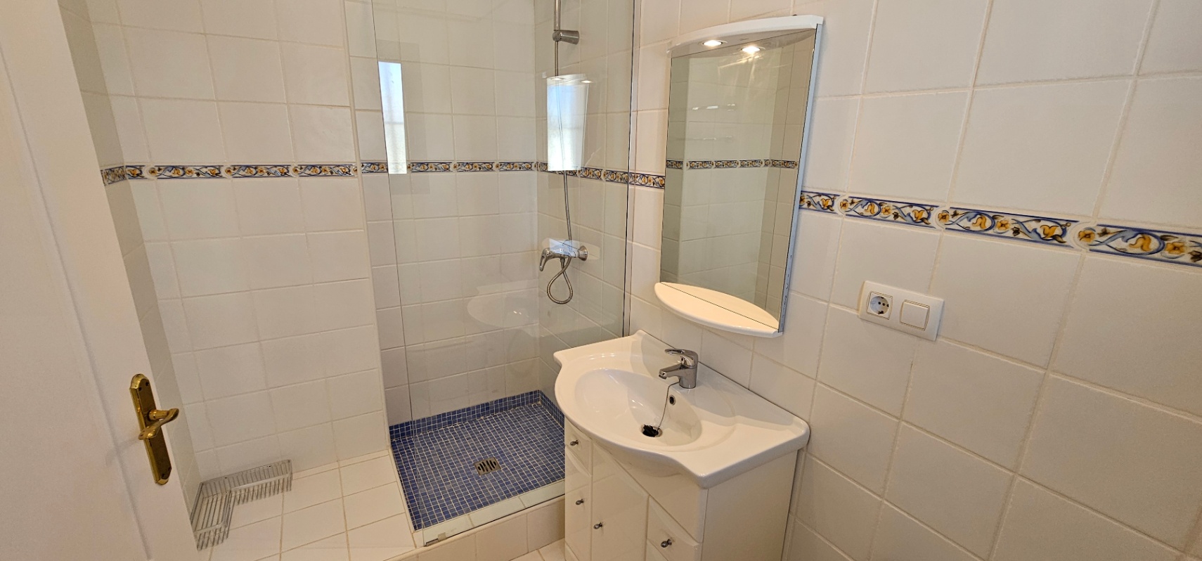 Functional bathroom featuring a walk-in shower with blue mosaic tiling, glass screen, white vanity unit, and illuminated mirror.
