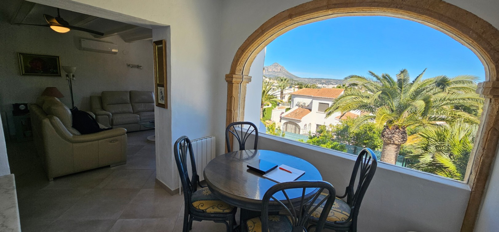 Glazed dining area featuring a traditional Tosca stone arch with views of the Montgó mountain. The space opens into a living room with leather seating and climate control.