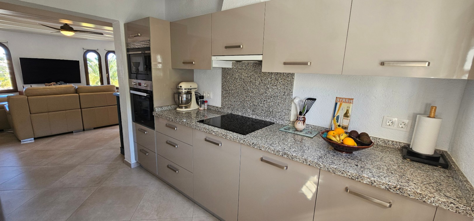 Independent kitchen featuring glossy taupe cabinetry, granite countertops, and integrated appliances, offering a direct view into the living area.