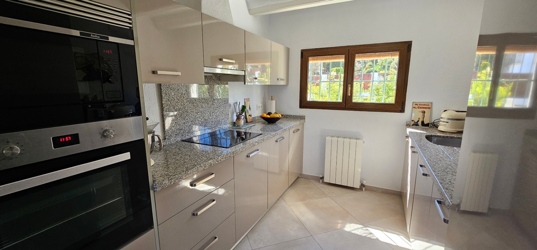 Independent kitchen featuring high-gloss cabinetry, granite countertops, and integrated appliances. A wooden-framed window provides natural light and garden views.