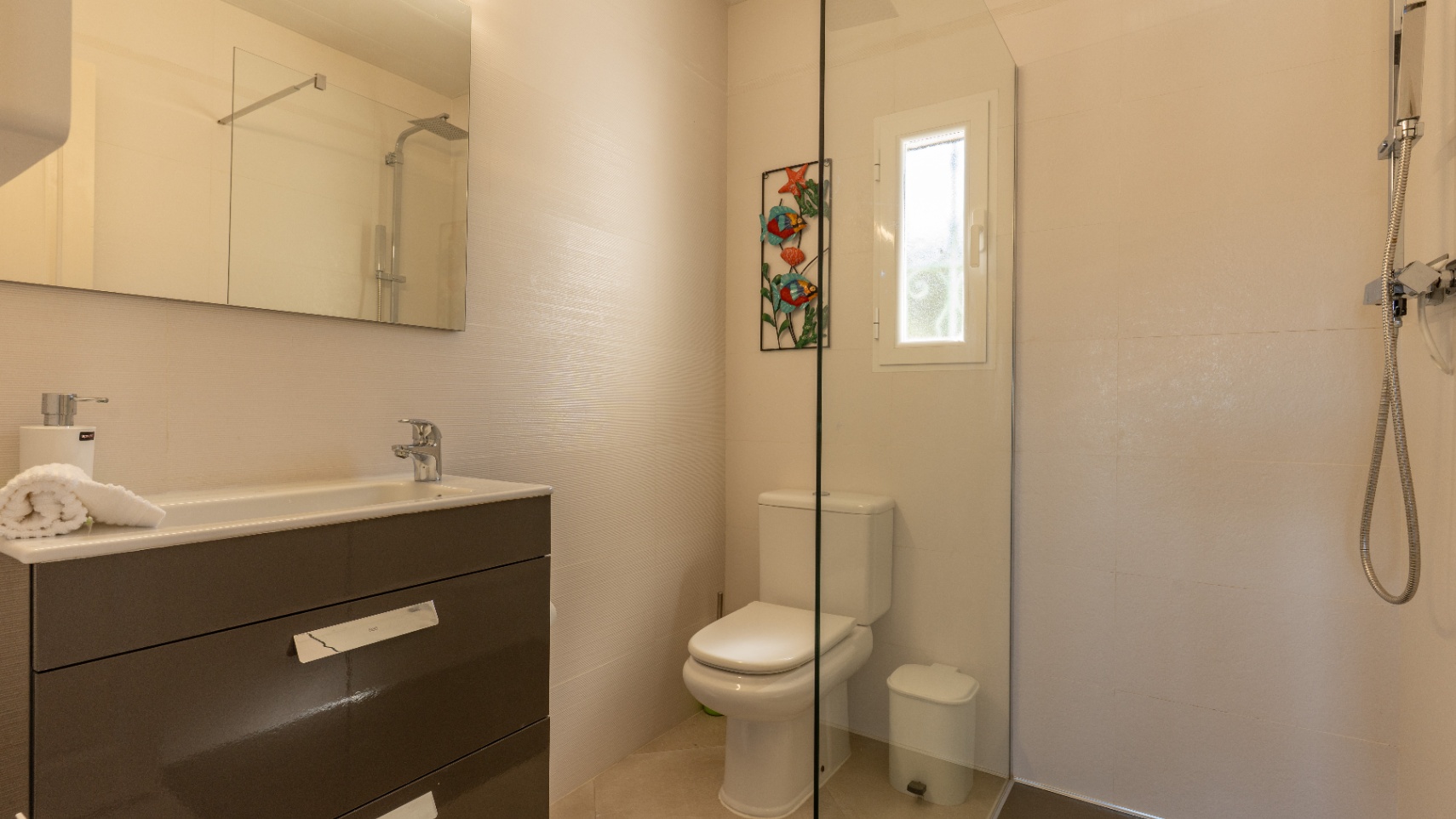 Modern bathroom featuring a dark grey vanity with integrated sink, large mirror, and walk-in shower with glass partition and chrome fixtures.