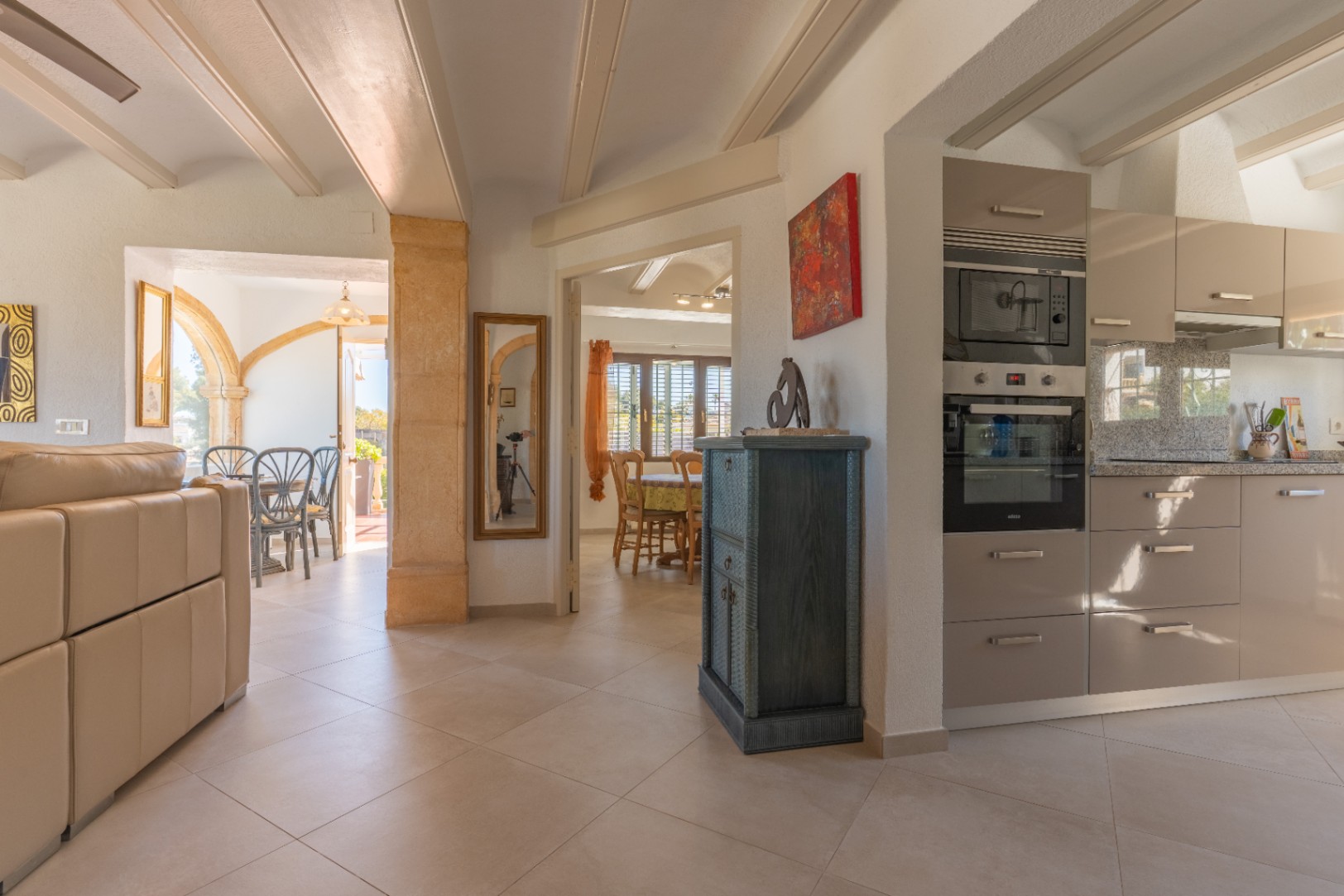 Open-plan living space featuring a modern kitchen with integrated appliances, beamed ceilings, and a traditional Tosca stone archway leading to the terrace.