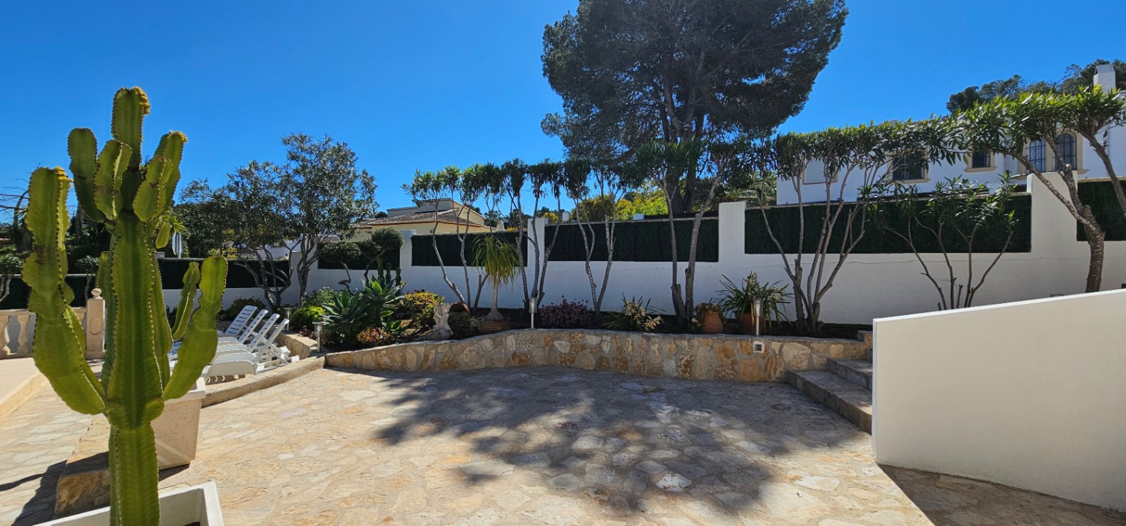 Outdoor terrace featuring natural stone paving, masonry retaining walls, and diverse Mediterranean landscaping with cacti and palm trees.