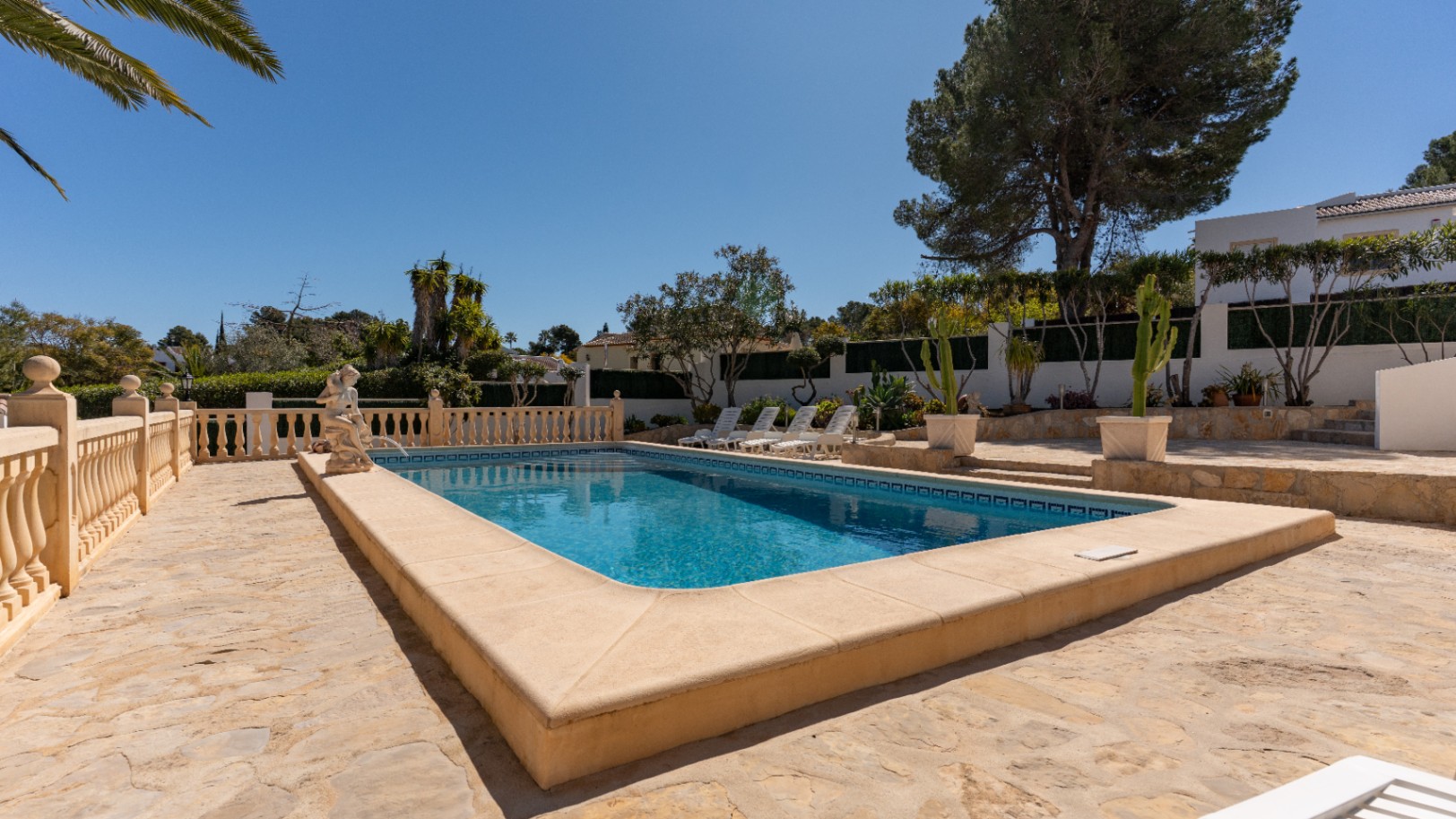 Rectangular swimming pool featuring a natural stone terrace, classic balustrades, and a sunbathing area surrounded by mature Mediterranean gardens.