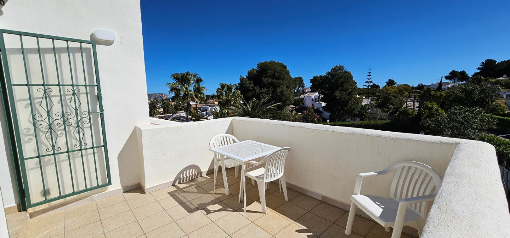 Upper-level open terrace featuring tiled flooring, white outdoor furniture, and panoramic views of the surrounding Mediterranean greenery and neighborhood.