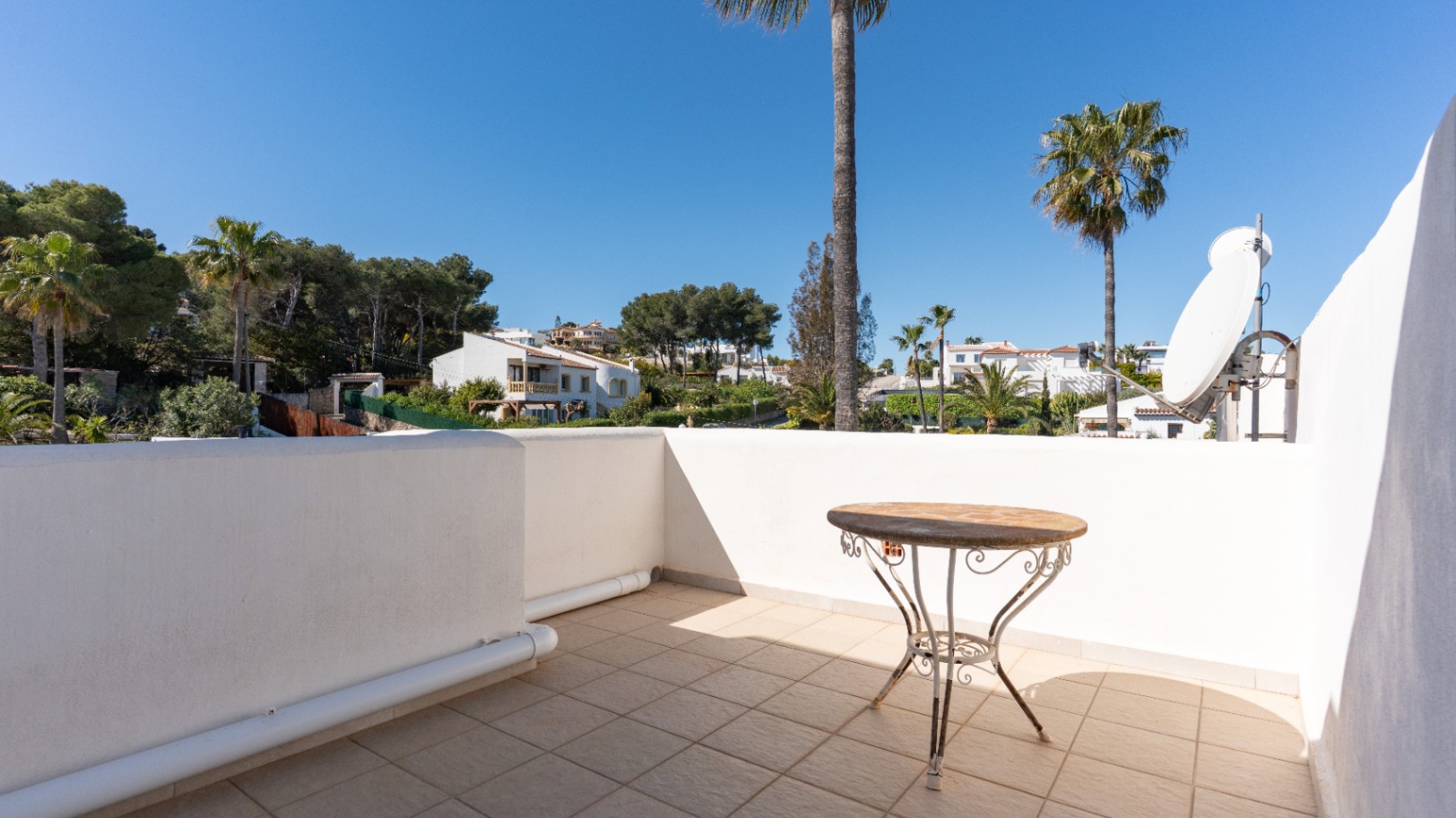 Upper terrace featuring tiled flooring, a wrought-iron side table, and a satellite dish, offering clear views of the surrounding Mediterranean landscape.