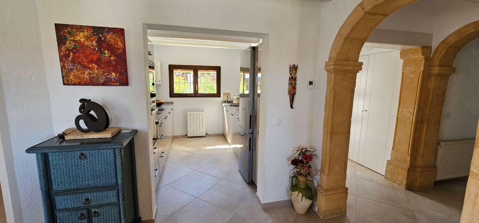 View from the living area towards the independent kitchen, featuring traditional Tosca stone arches and large ceramic floor tiles.