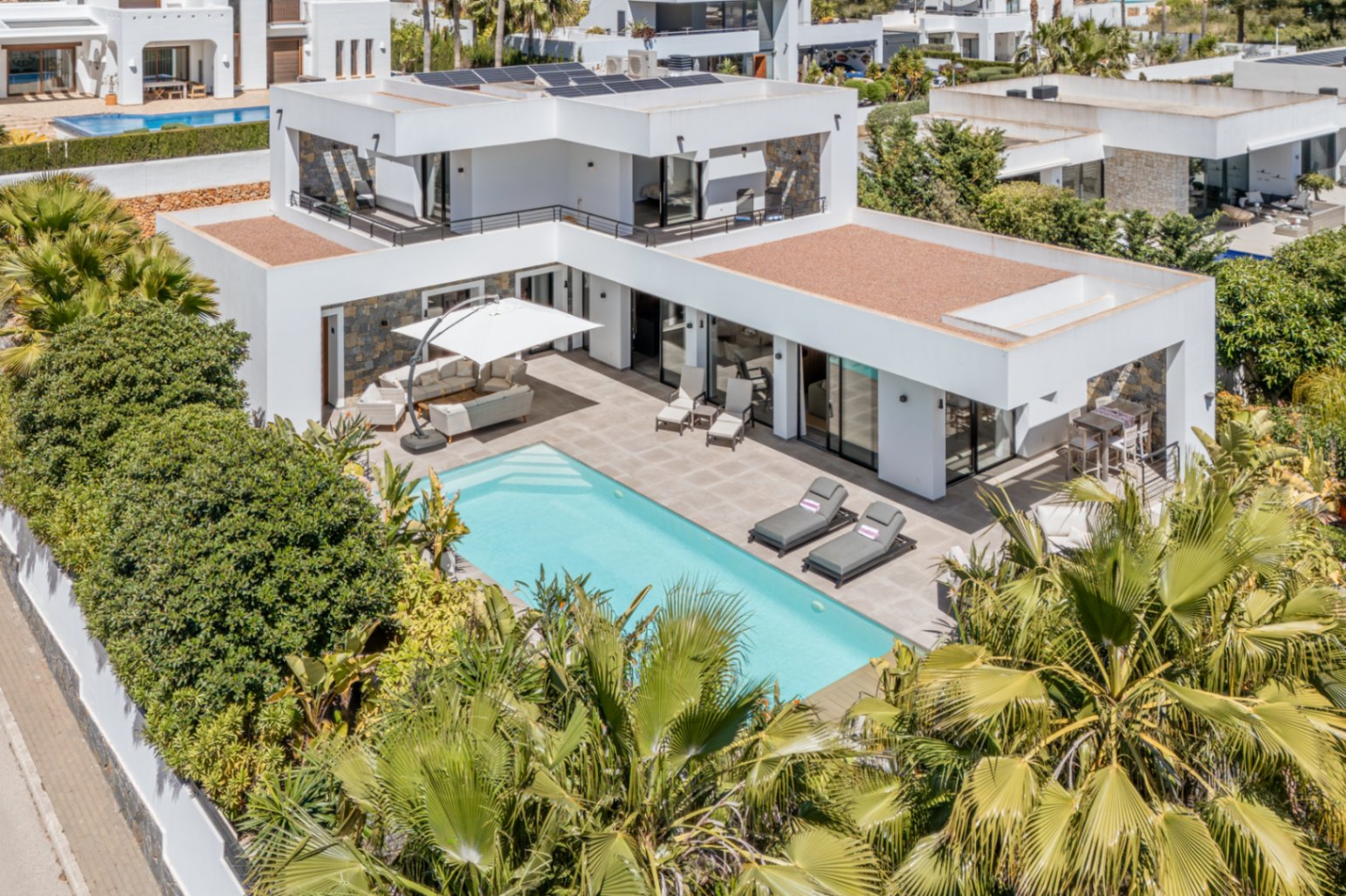 Aerial view of the modern villa featuring a private pool, rooftop solar panels, and spacious terraces framed by mature Mediterranean gardens.