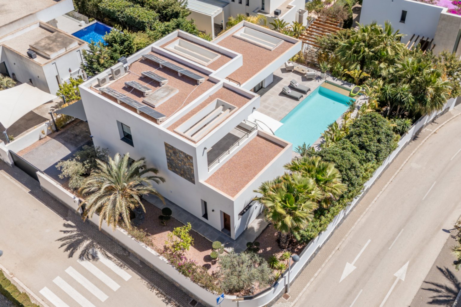 Aerial view of the modern villa featuring rooftop solar panels, a private swimming pool with sun terrace, and mature Mediterranean landscaping on a corner plot.