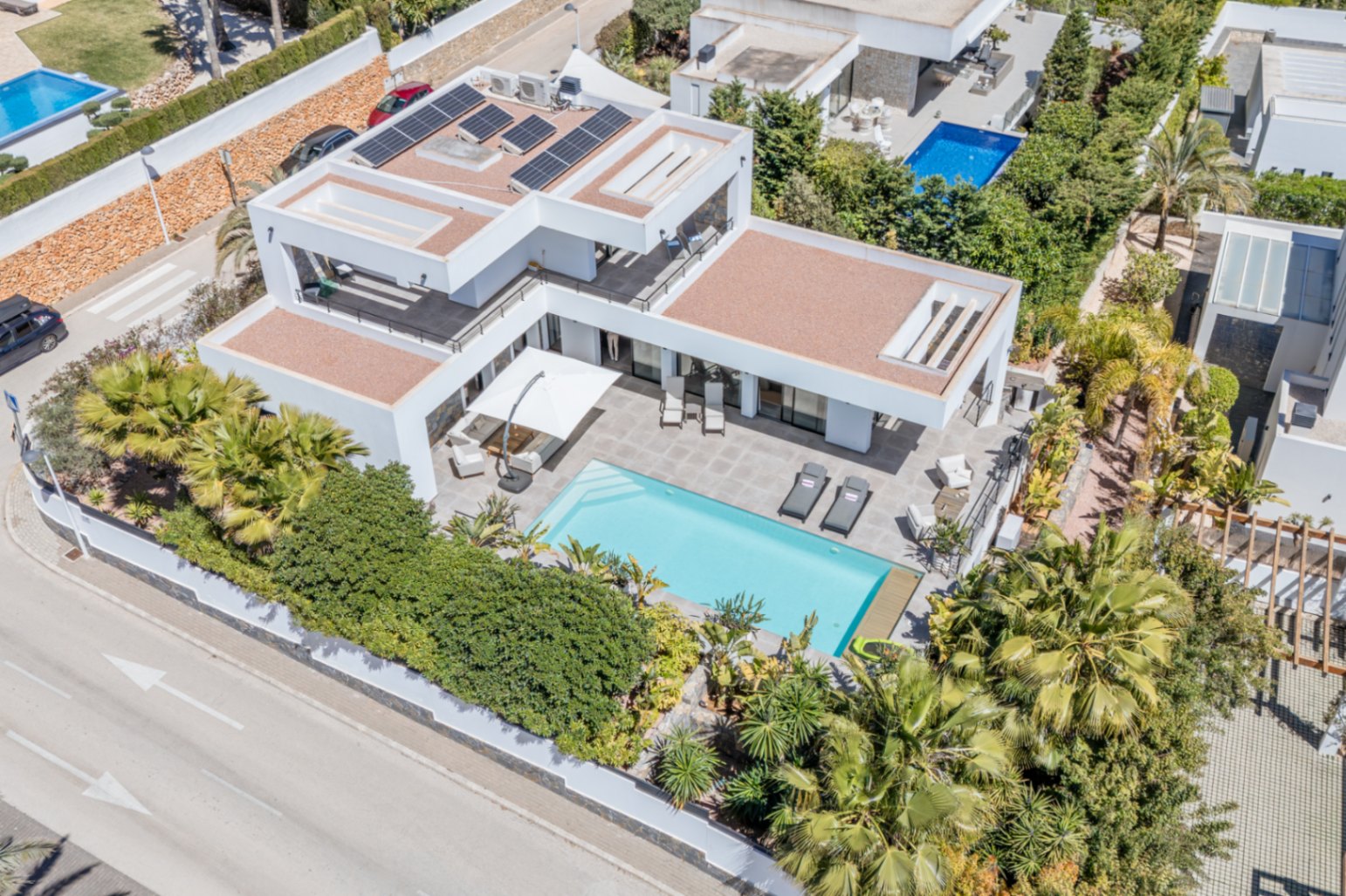 Aerial view of the modern villa featuring rooftop solar panels, a rectangular swimming pool, and expansive terraces bordered by mature Mediterranean gardens.