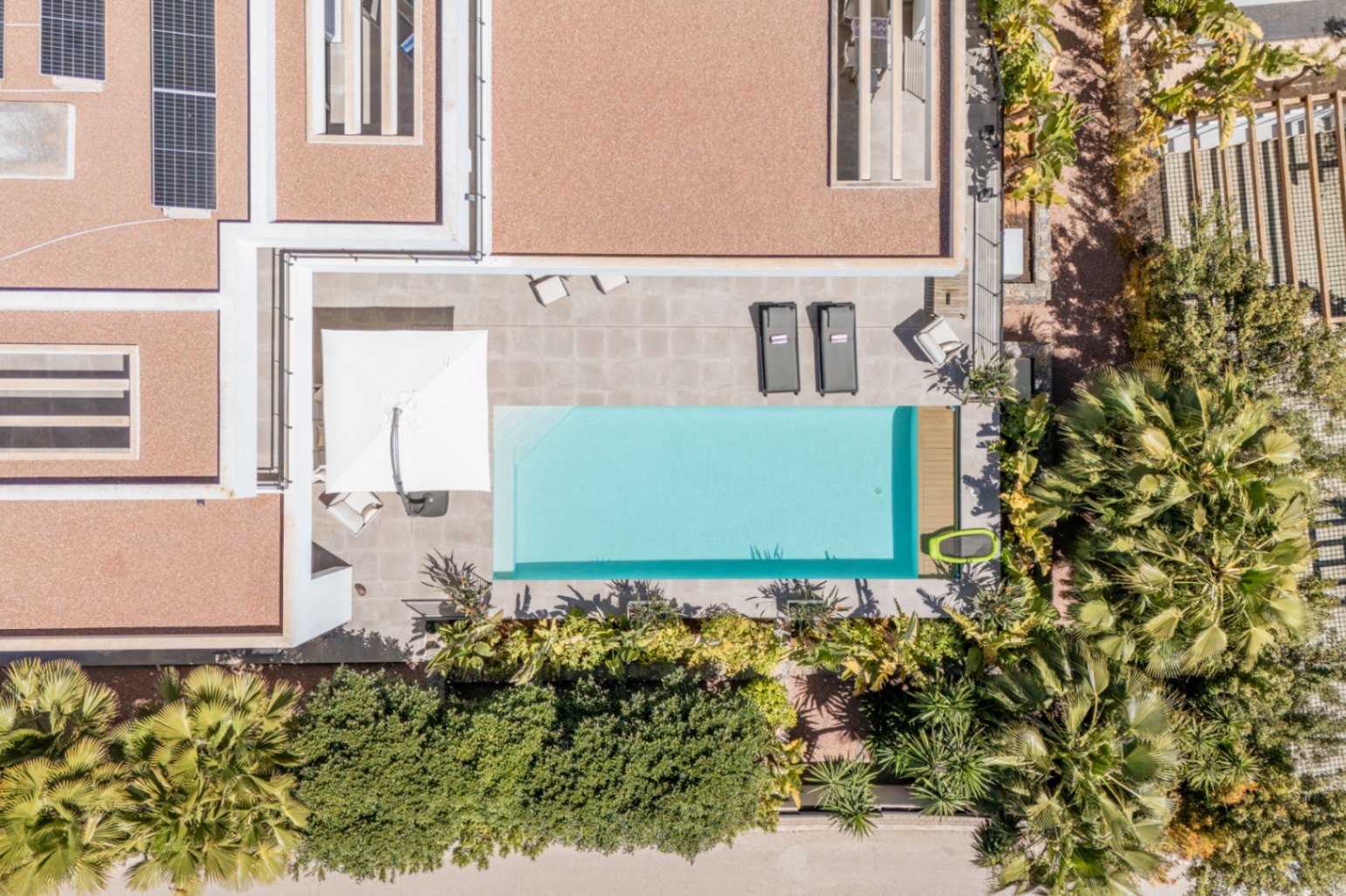 Aerial view of the rectangular swimming pool and stone-tiled terrace, featuring roof-mounted solar panels and lush perimeter landscaping.