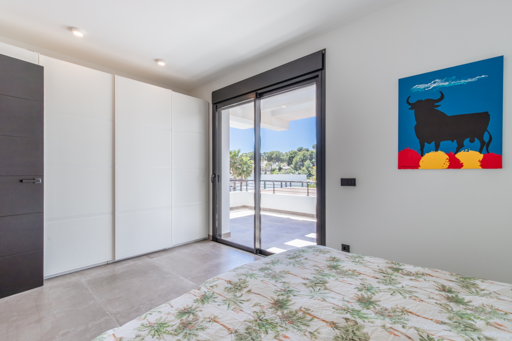 Bedroom featuring minimalist white built-in wardrobes and sliding glass doors that open onto a private upper-floor terrace with open views.