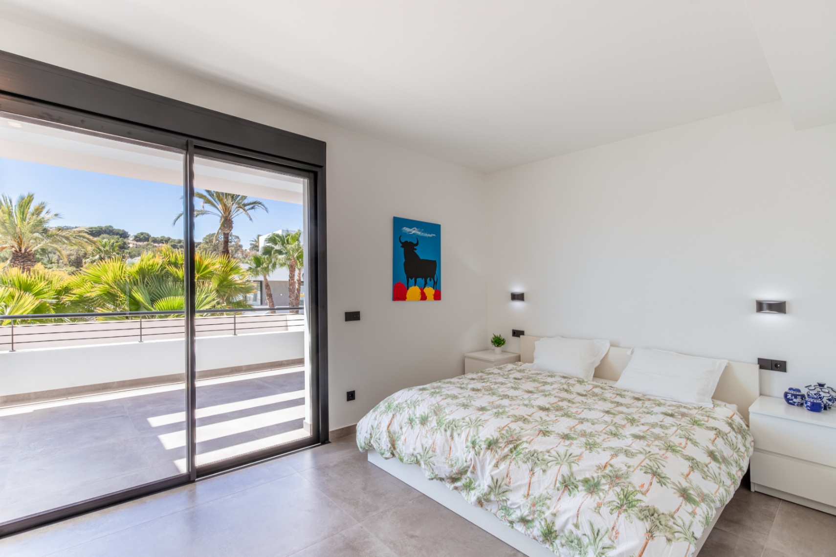 Bright bedroom featuring direct access to a private terrace through large sliding glass doors. Grey tiled flooring and minimalist decor with integrated wall lighting.