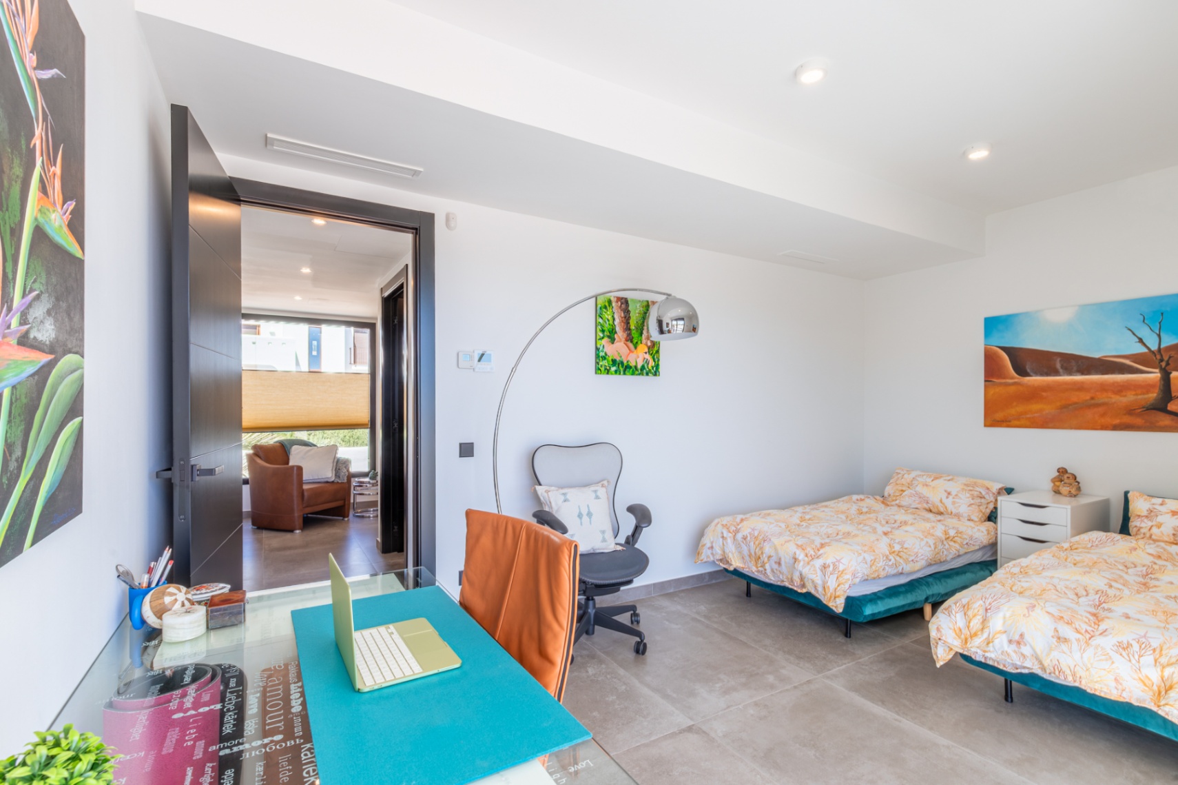 Bright bedroom featuring twin beds, an integrated workspace with a glass desk, and large-format porcelain flooring. Recessed ceiling lights and clean white walls enhance the space.