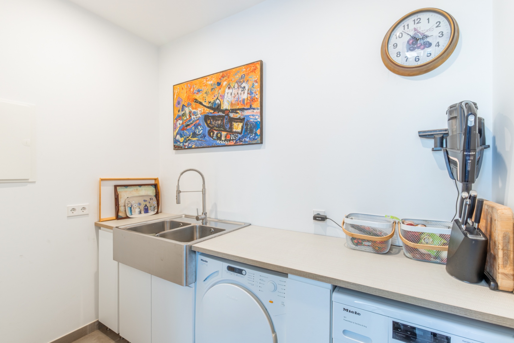 Functional laundry room featuring premium Miele appliances, a deep double stainless steel sink, and a spacious neutral countertop with integrated storage.