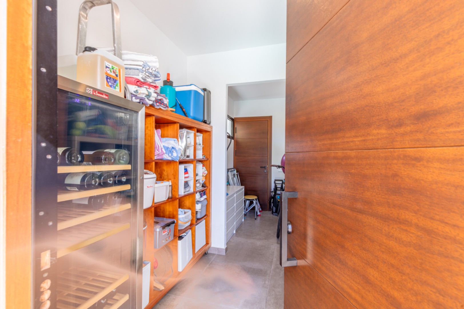 Functional utility room and pantry featuring custom wood shelving, a professional wine cooler, and direct access through high-quality wooden doors.