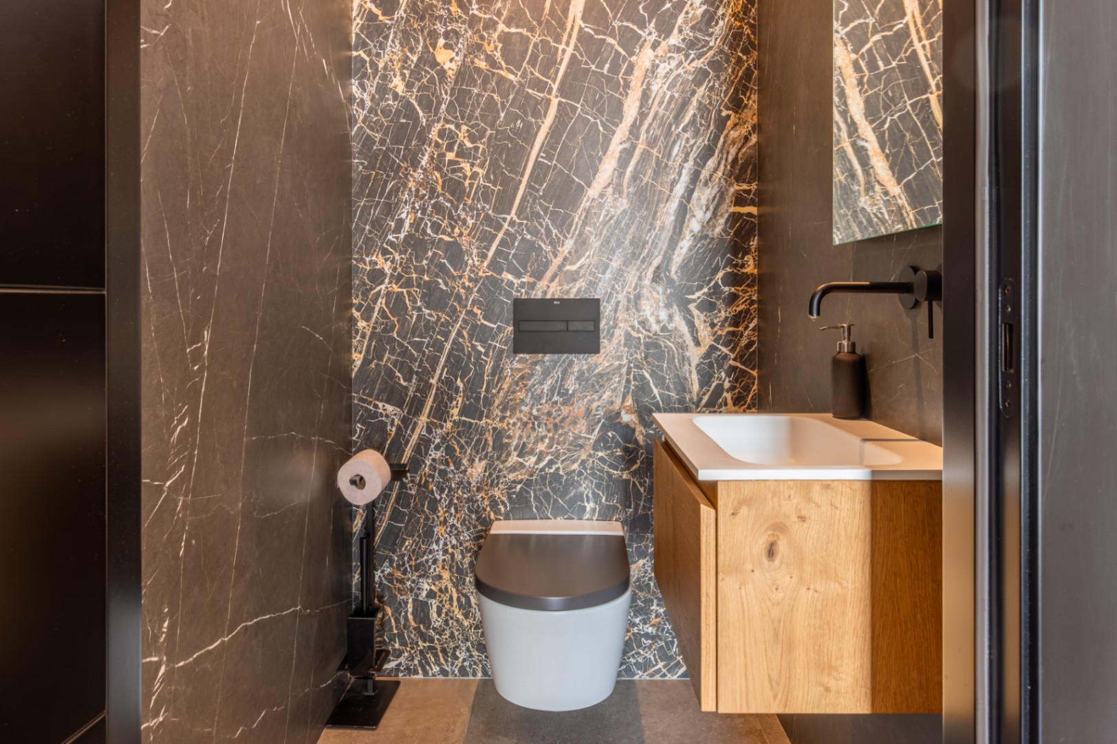 Guest toilet featuring a dramatic dark marble accent wall with gold veining, a wall-hung toilet, and an oak vanity with matte black fixtures.