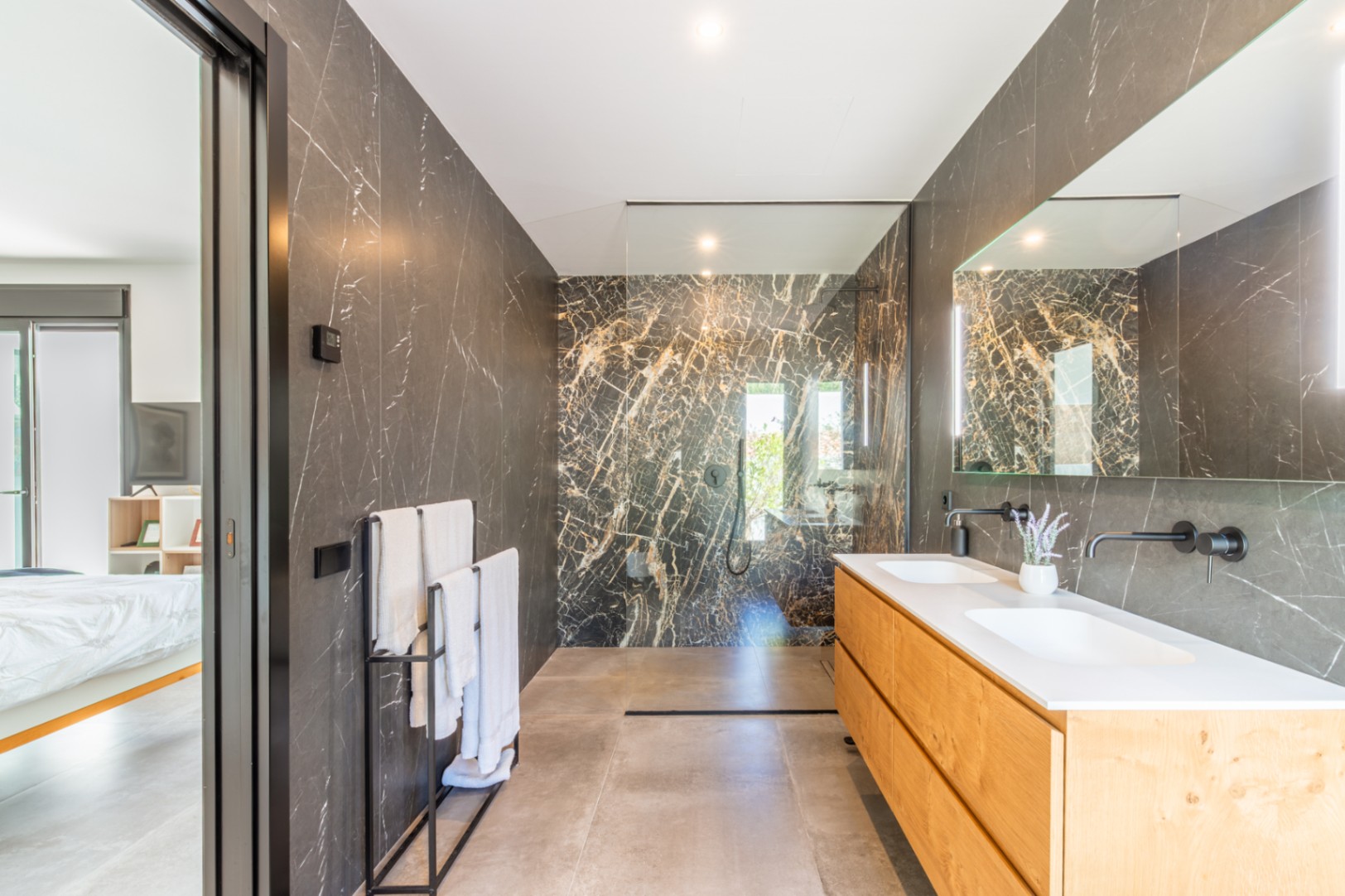 Master bathroom featuring dark marble walls, a double wooden vanity with black wall-mounted faucets, and a spacious walk-in shower.