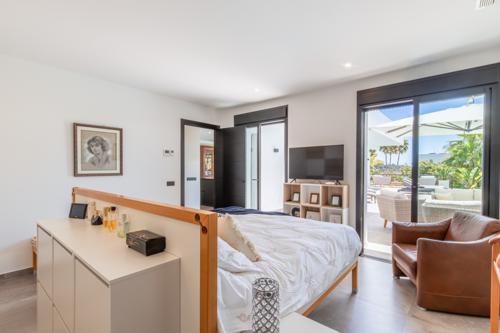 Master bedroom featuring direct terrace access through large sliding glass doors, integrated storage partitions, and abundant natural light with garden views.