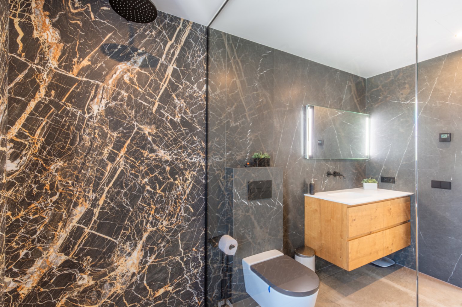 Modern bathroom featuring a walk-in rain shower, dark marble-effect wall tiles, a floating wooden vanity, and a sleek backlit mirror.