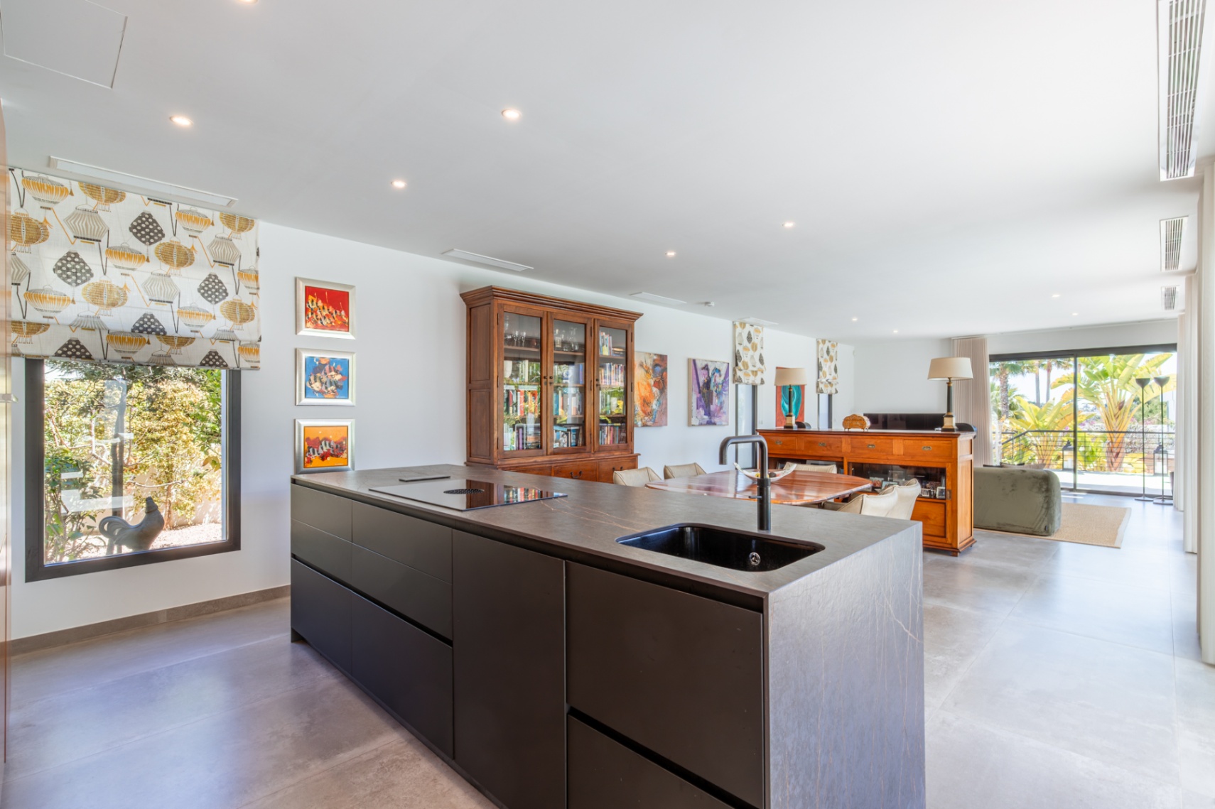 Modern kitchen featuring a dark stone island with integrated sink and induction hob, opening into a bright living area with direct terrace access.